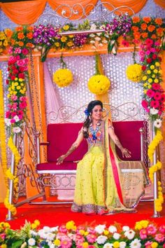 a woman sitting on top of a red couch in front of yellow and pink flowers