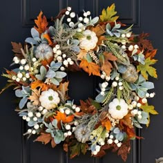 a wreath with white pumpkins and greenery hangs on a black front door,