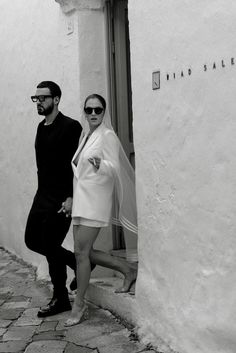 a man and woman standing next to each other in front of a white building with windows