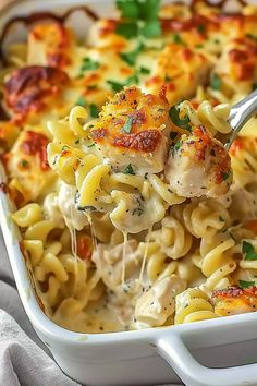 a spoon full of chicken and pasta casserole being lifted from the casserole dish