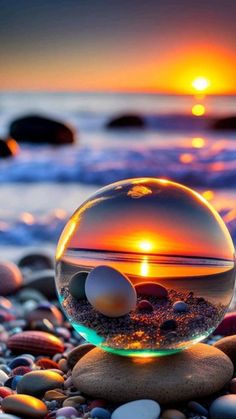 a glass ball sitting on top of a pile of rocks next to the ocean at sunset