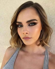 a woman with dark makeup and brown eyes wearing grey tank top, looking at the camera