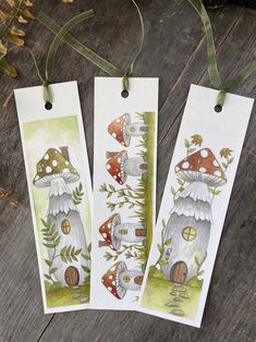 three bookmarks with mushrooms on them hanging from green ribbon and some plants in the background