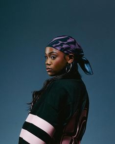 a woman wearing a black and pink top with a bandana on her head standing in front of a blue background