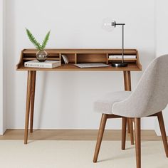 a desk with a chair, lamp and books on it in front of a white wall