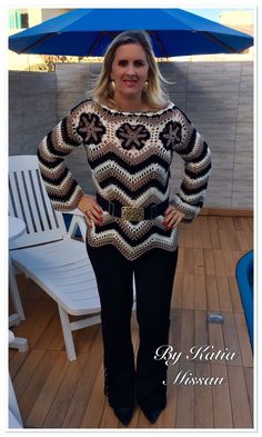 a woman standing in front of an umbrella wearing black pants and a sweater with flowers on it