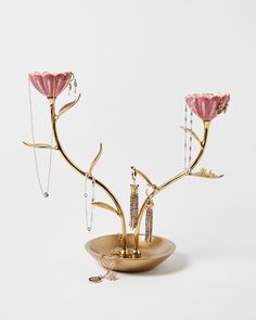 a gold plate with pink flowers on it and jewelry hanging from the top, in front of a white background