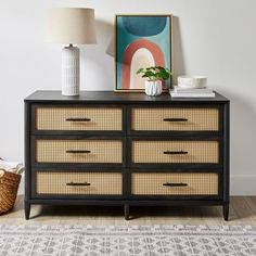 a black dresser with wicker drawers and a white vase sitting on top of it