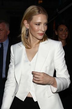 a woman in a white blazer and black pants is seen walking down the street