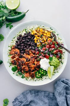 a white bowl filled with rice, black beans, corn and avocado next to cilantro