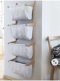 three white baskets are hanging on the wall next to a wooden chair and a black and white striped pillow