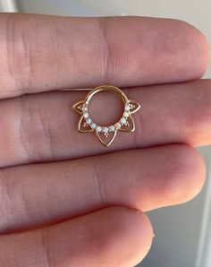 a person's hand holding a small gold nose ring with pearls on the end