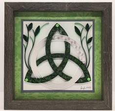 an intricate paper art piece with green and white designs in a wooden frame on the wall