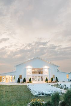 a white barn with rows of chairs in front of it and the sky above them