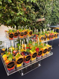 an assortment of fruit is displayed in plastic containers on a table outside with trees and bushes behind it