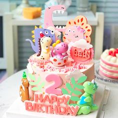 a birthday cake with dinosaurs and other decorations on the top is decorated in pink, green, yellow and blue