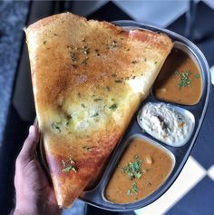 a person holding a plate with some food in it and dipping sauces on the side