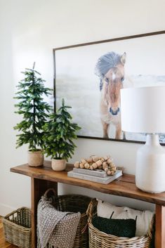 a wooden table topped with baskets next to a christmas tree and a painting on the wall