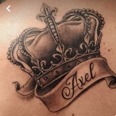 the back of a woman's shoulder with a crown and banner tattoo on it