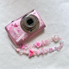 a pink camera sitting on top of a table next to a beaded lanyard