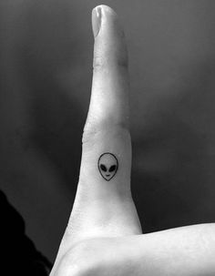 an alien head tattoo on the middle of someone's left hand, with black ink