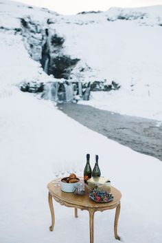 two bottles of wine sitting on top of a table in the snow next to a waterfall