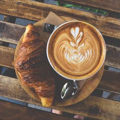 a cup of coffee and croissant on a wooden table