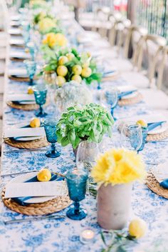 a long table is set with blue and yellow place settings, lemons in vases