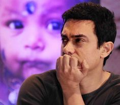 a man sitting in front of a purple background with his hand on his chin and looking at the camera