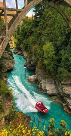 a red boat traveling down a river under a bridge