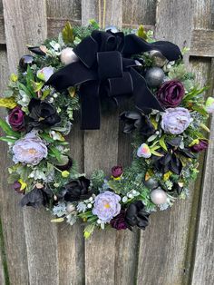 a wreath with black and purple flowers hanging on a wooden fence next to a metal ornament