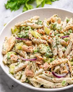 a white bowl filled with chicken salad and garnished with red onions, cucumbers, and limes