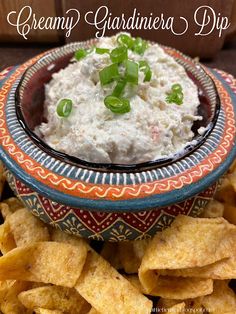 a bowl filled with cream cheese dip surrounded by tortilla chips and green onions