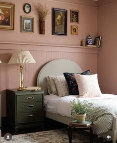 a bedroom with pink walls and pictures on the wall above the bed, along with a green dresser