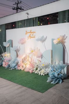 an artificial flower display in front of a white wall with blue and pink flowers on it