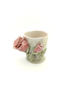 a white cup with pink roses painted on the outside and inside, sitting in front of a white background