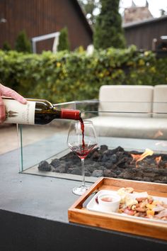 a person pouring wine into a glass next to a fire pit with food on it