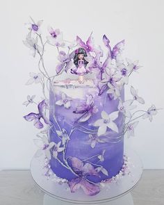 a purple cake with white flowers and a fairy on top