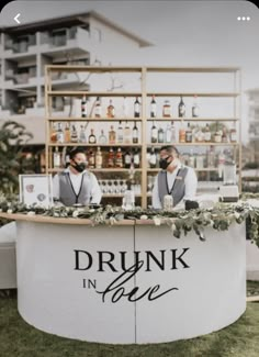 two men standing behind a bar with drinks on it