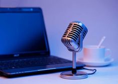 a laptop computer sitting on top of a desk next to a microphone and coffee cup