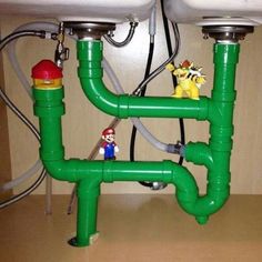 two green pipes connected to each other in front of a sink with mario and luigi figurines on them