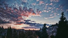 the sun is setting behind some clouds in the sky over houses and trees on a hill