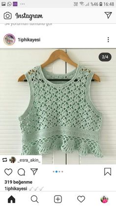 a green top with crocheted details on the front and back, hanging from a wooden hanger