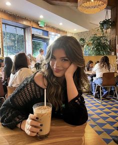 a woman sitting at a table with a drink in her hand and looking into the camera