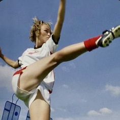 a woman in white shirt and red socks kicking a soccer ball with her leg up