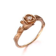 a gold ring with a diamond in the center and leaves on each side, against a white background