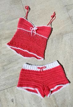 a red and white crocheted swimsuit laying on the ground next to a pair of shorts