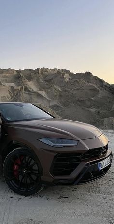 a man standing next to a brown sports car on top of a sandy hill side