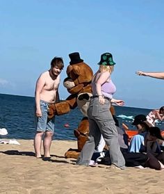 three people standing on the beach with a large teddy bear in front of them,