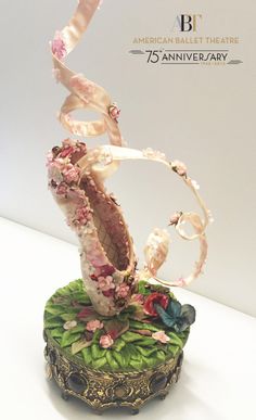 a sculpture with flowers and ribbons on top of it's base in front of a white wall